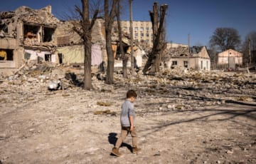 破壊された学校の前を歩くウクライナの子ども（2022年3月、AFP＝時事）