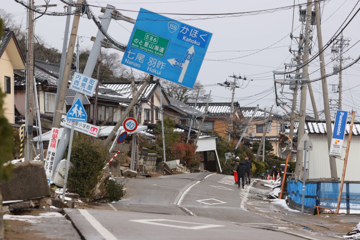 能登半島地震の発生後、液状化とみられる影響で波打つ道路と傾いた家や電柱（1月16日、石川県内灘町、時事通信フォト）